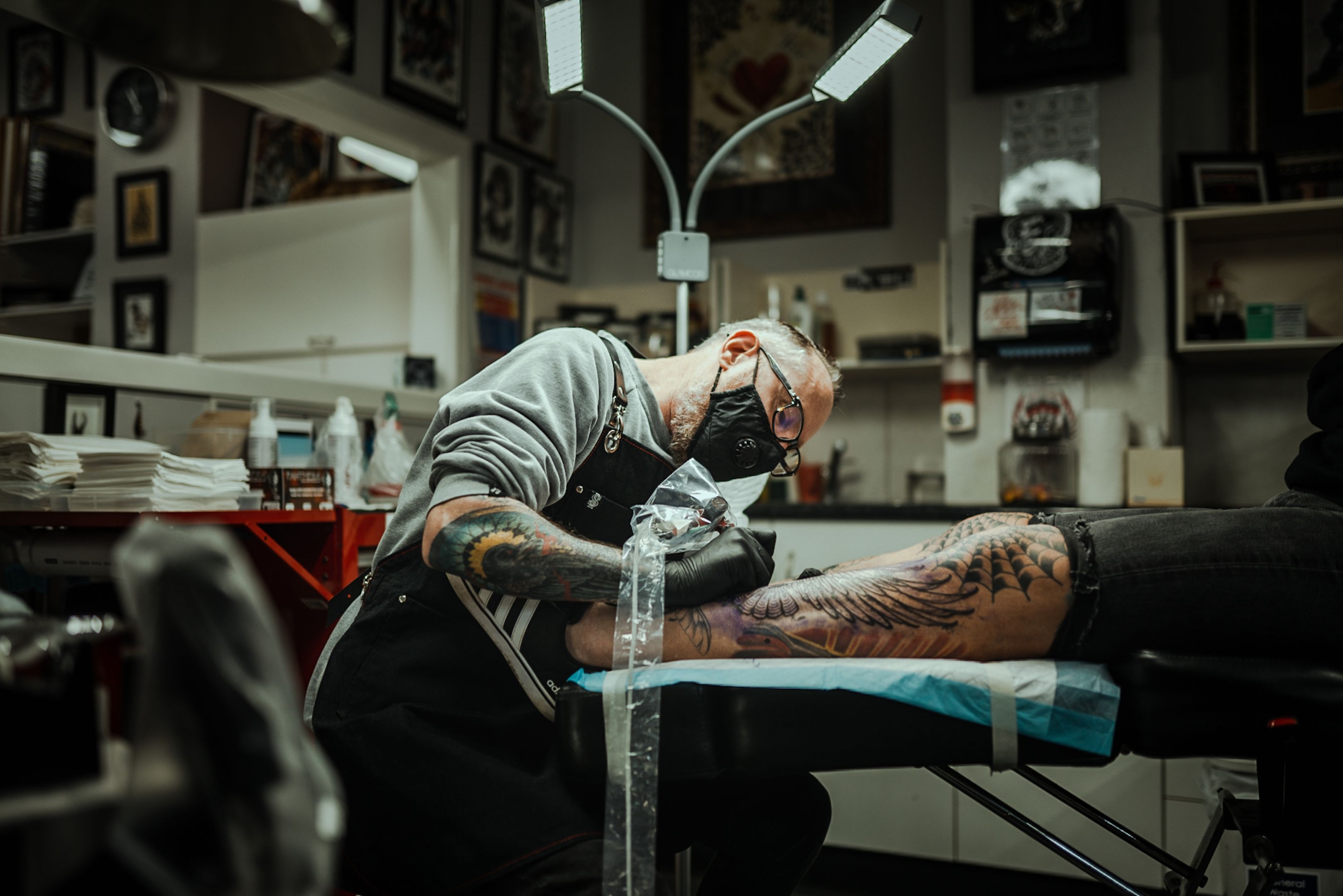 A resident artist shading a black-and-grey eagle across a client's leg.